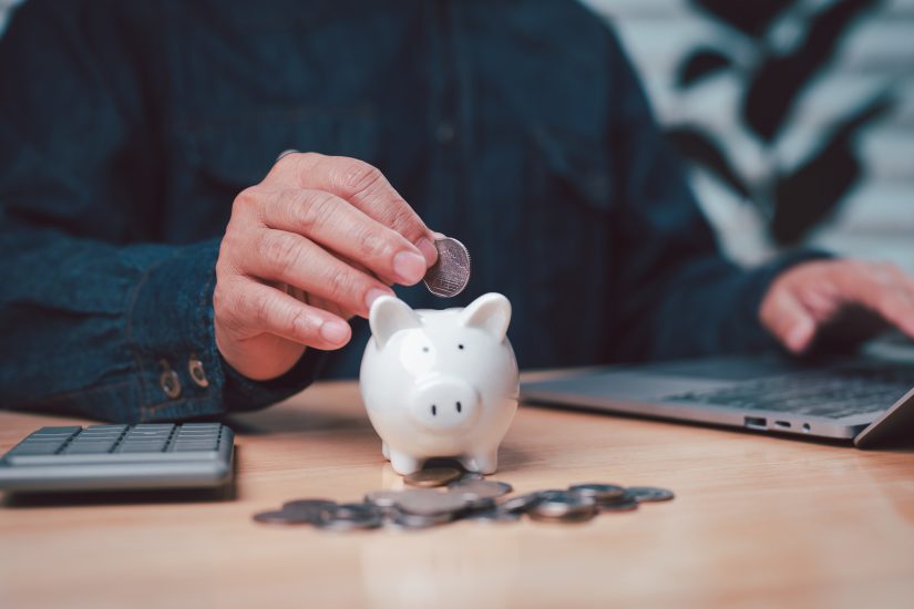 persons hand deposits a coin into piggy bank