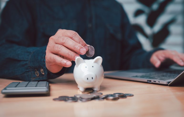 persons hand deposits a coin into piggy bank